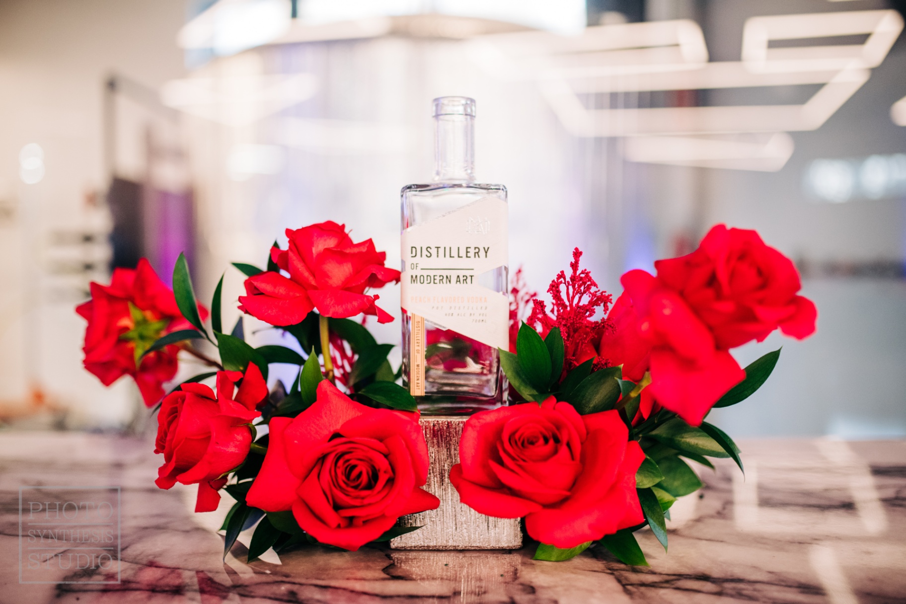 Crimson rose halo around a Distillery of Modern Art peach vodka bottle on veined marble