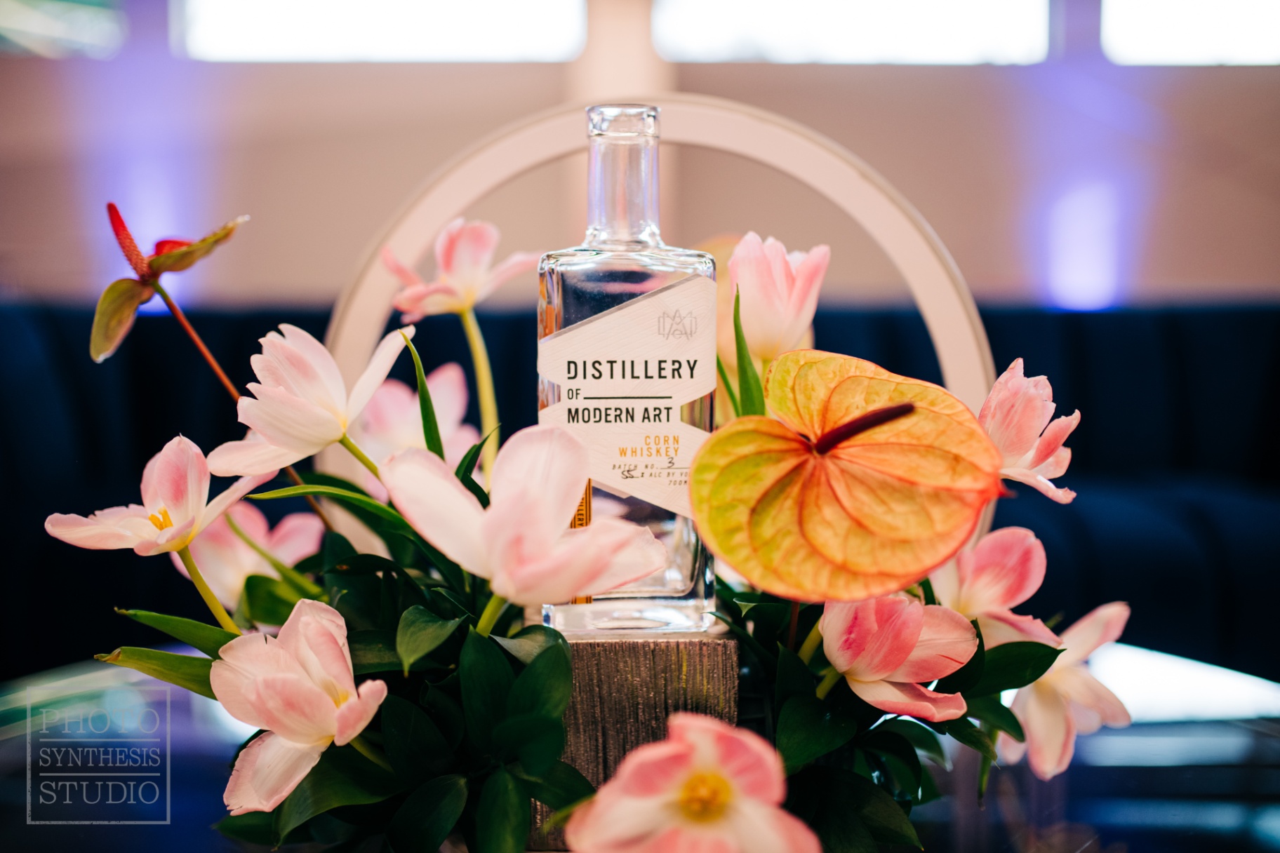 Distillery of Modern Art corn whiskey bottle nested in pink tulips and peach anthurium