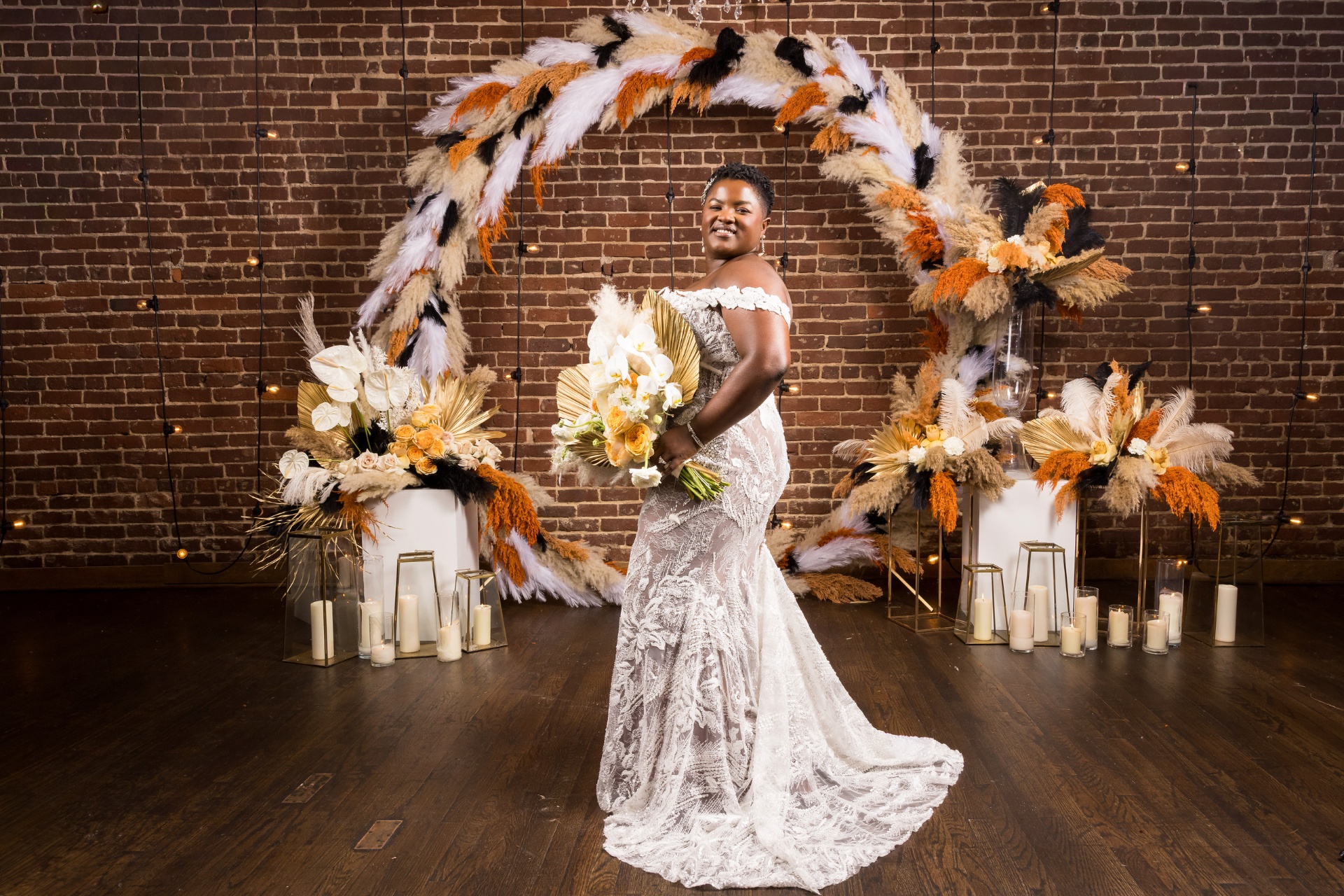 Bride in lace gown with cascading orchid and gilded palm bouquet beside the feather halo arch