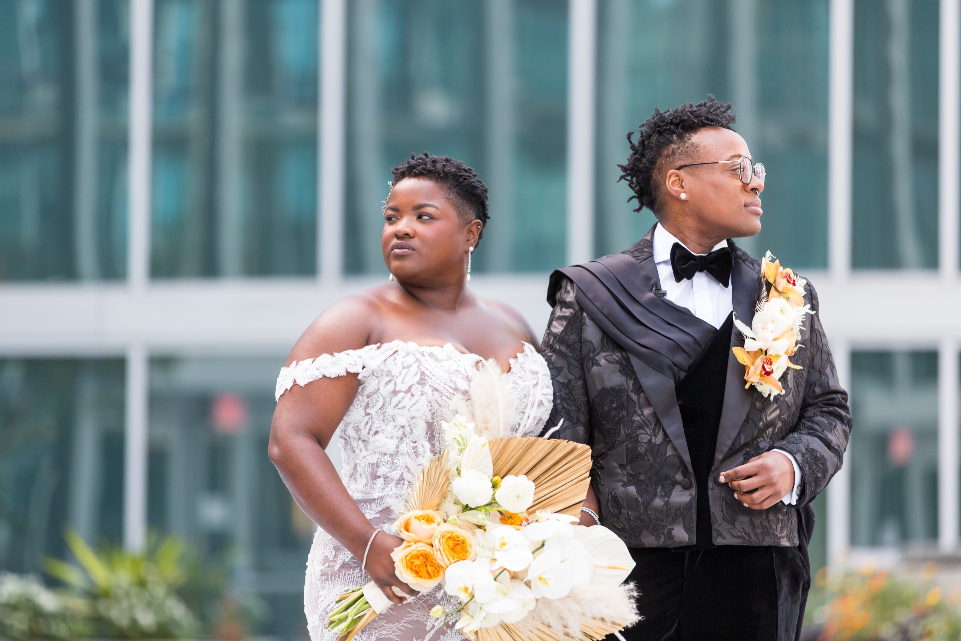 Newlyweds back to back outdoors with lace gown, brocade tuxedo and orchid bouquet