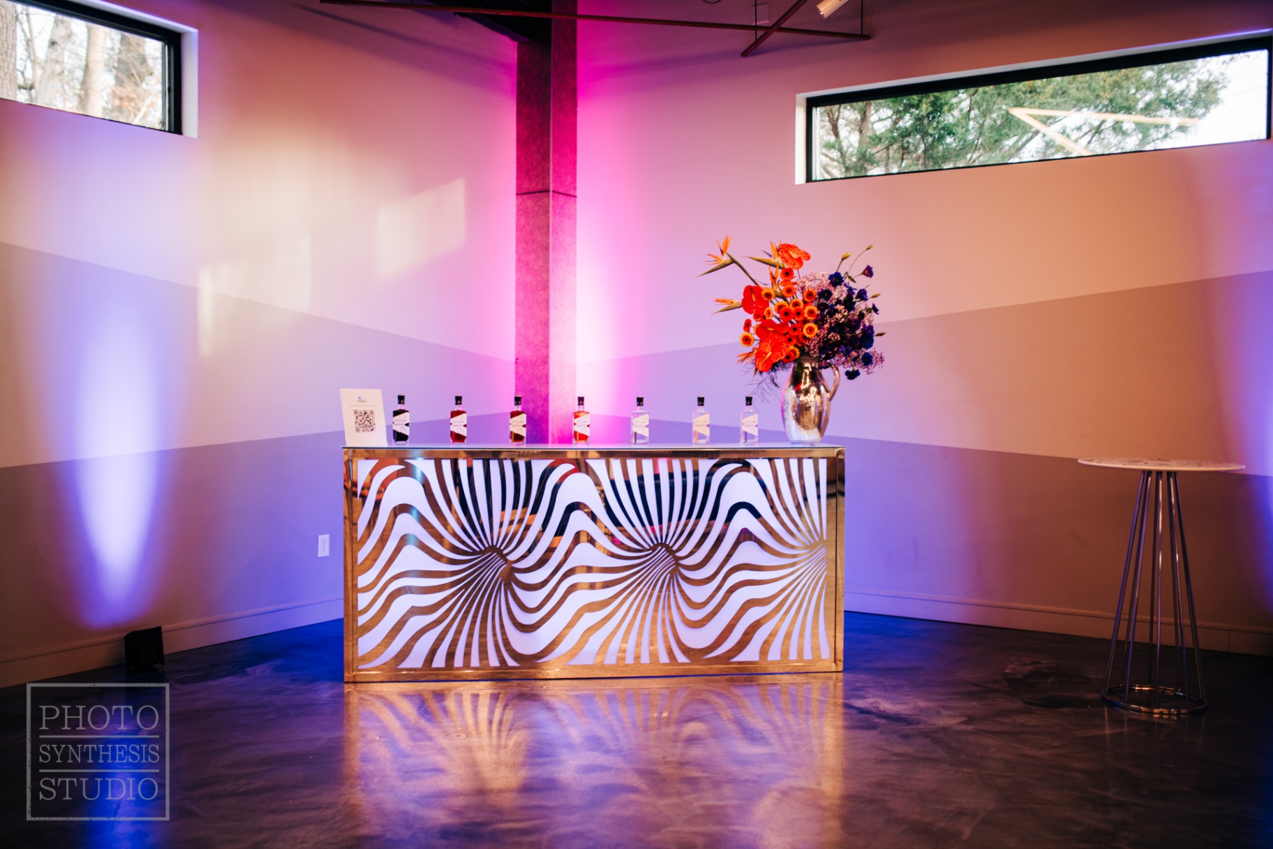 Op-art swirl-front bar lined with Distillery of Modern Art bottles under magenta wash