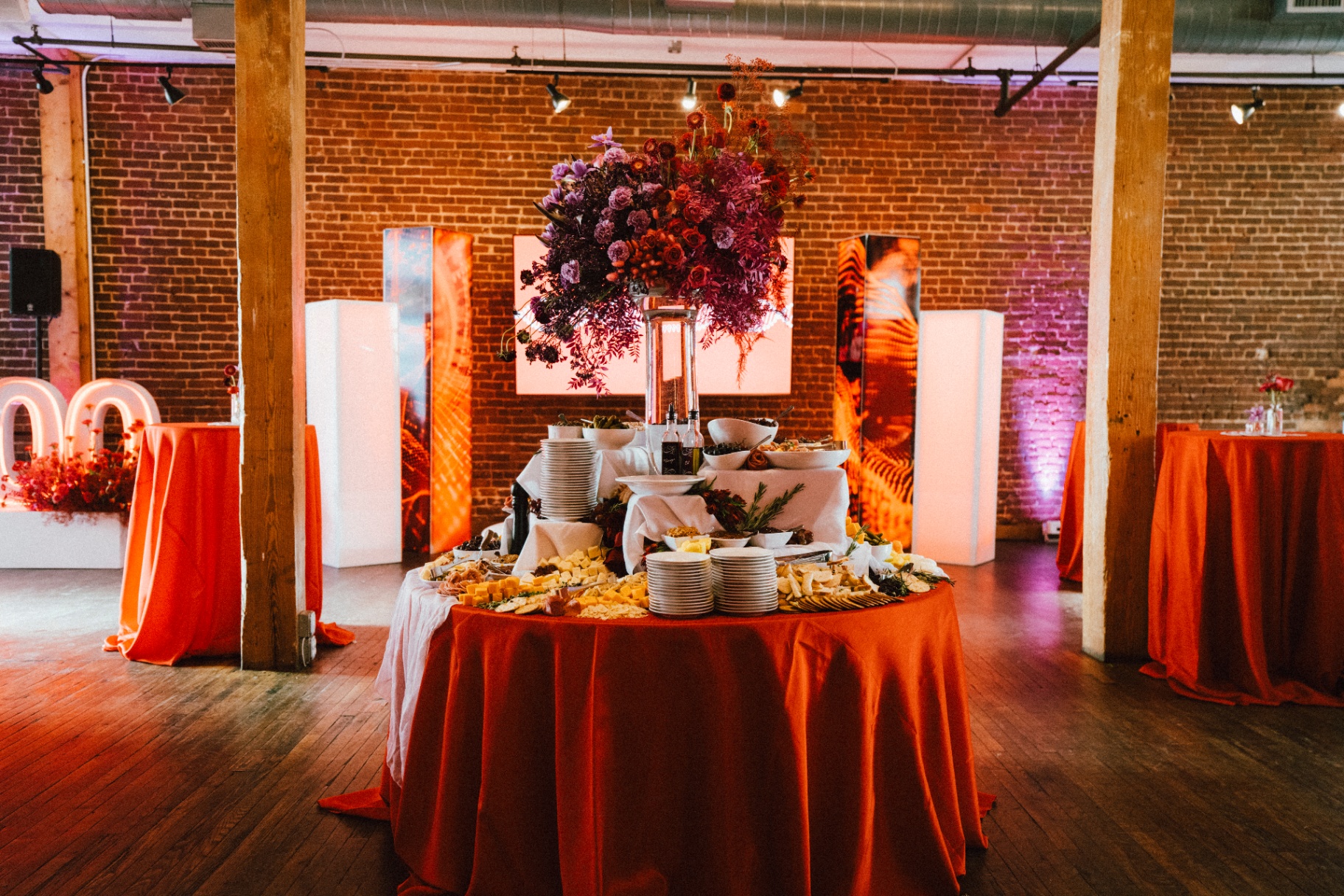 Towering jewel-toned floral centerpiece on a scarlet linen grazing table in a brick loft