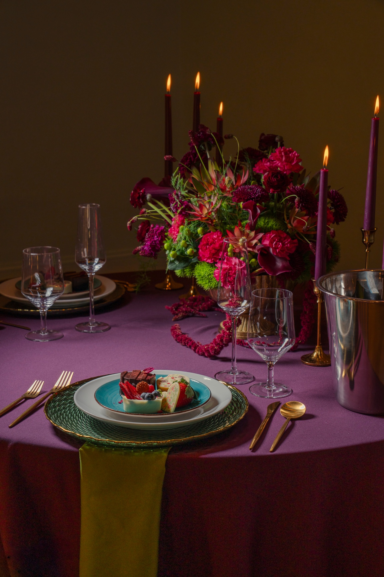 Footed urn overflowing with magenta carnations, protea, calla lilies and chartreuse foliage in candlelight