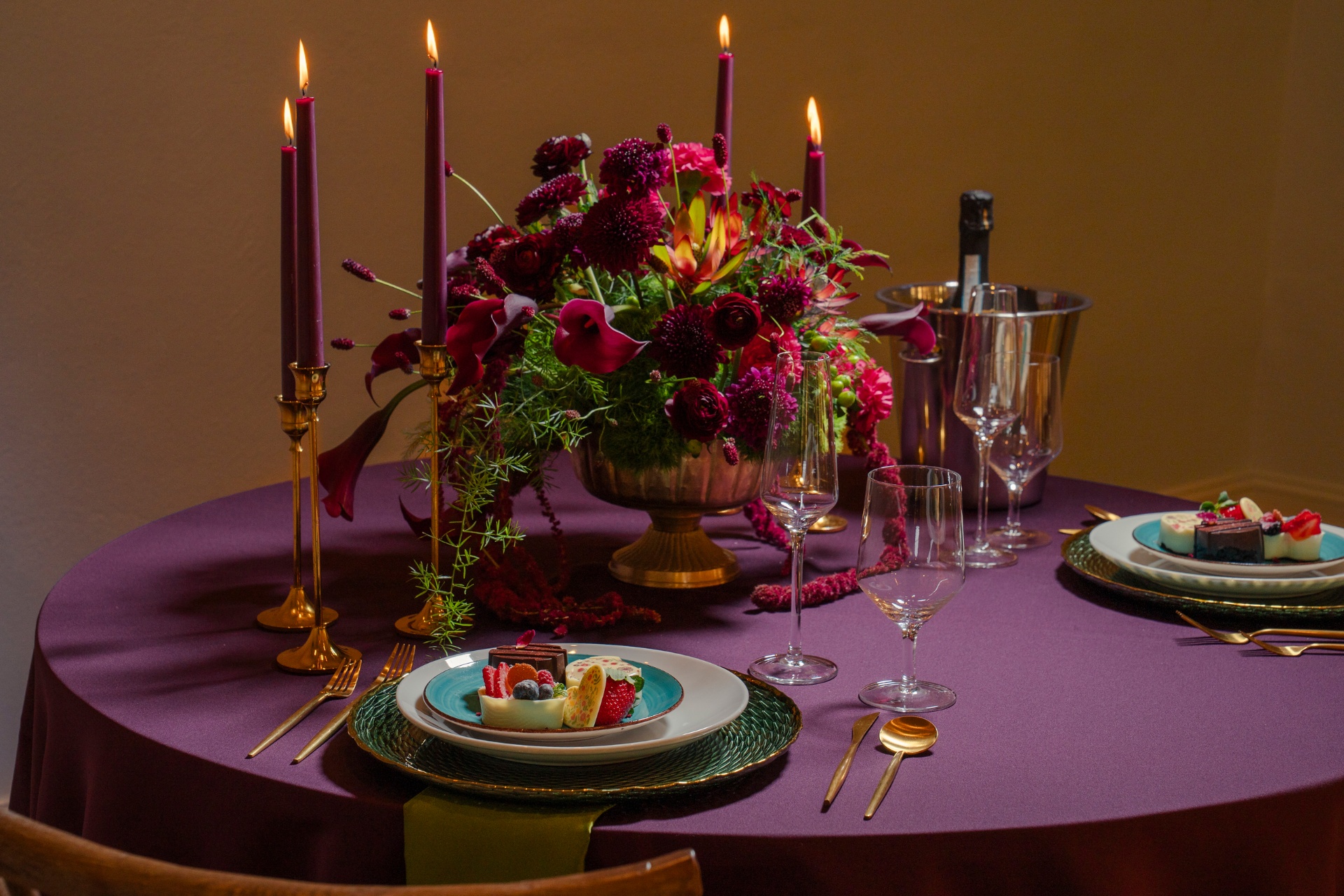 Gilt-edged green charger, turquoise plate and dessert vignette beside a crimson floral centerpiece