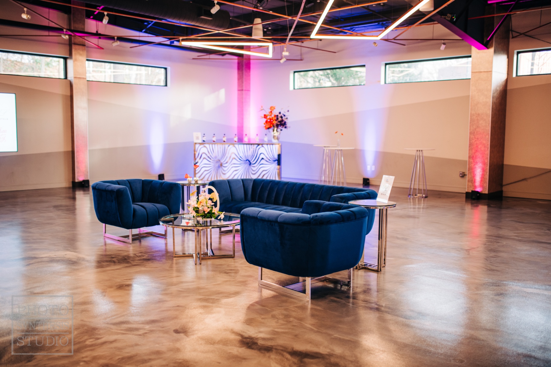 Navy velvet lounge configuration under linear pendants with bar and floral moment beyond