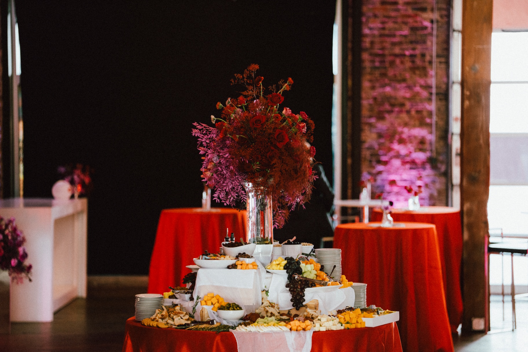 Crimson rose and dyed foliage tower over a scarlet grazing table in magenta light